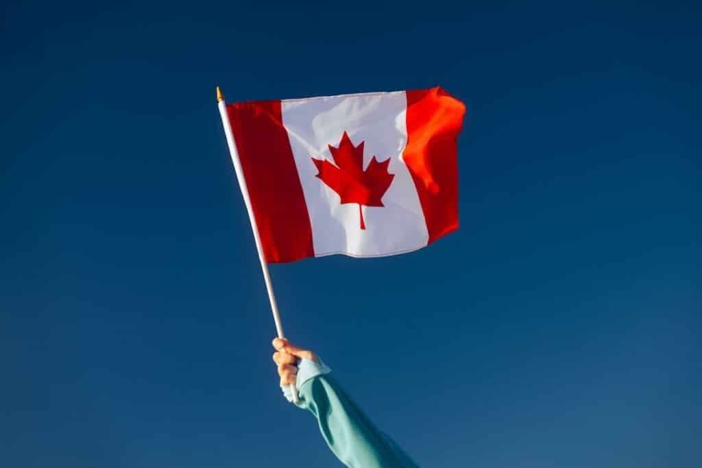 A hand holding up a Canadian flag against a blue sky.